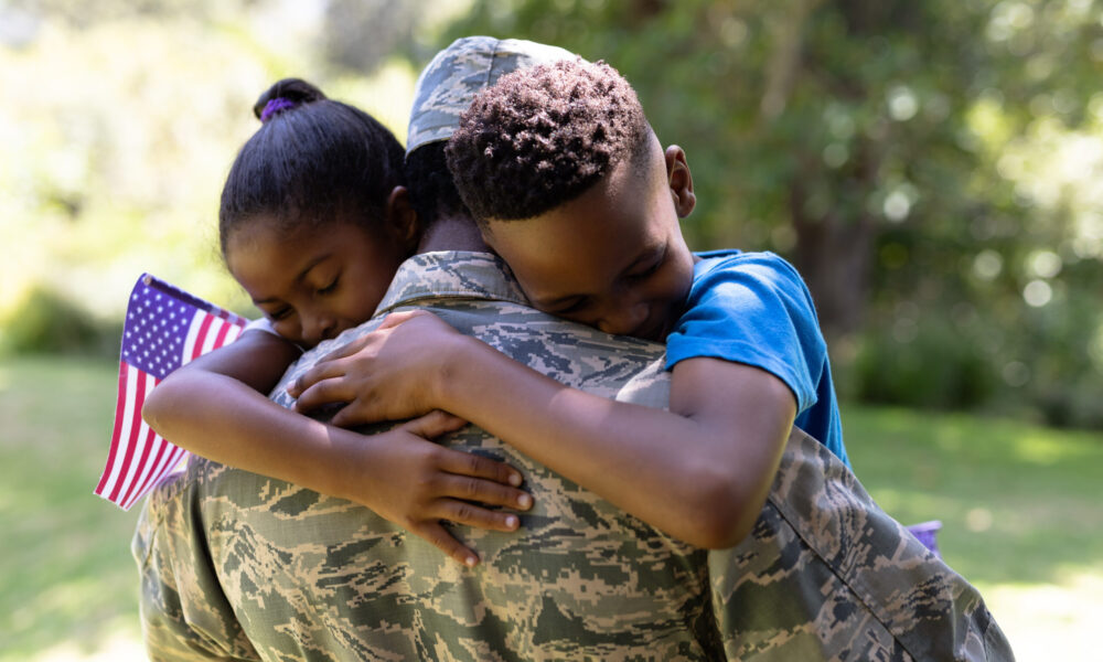 soldier hugging his two young children holding American flag