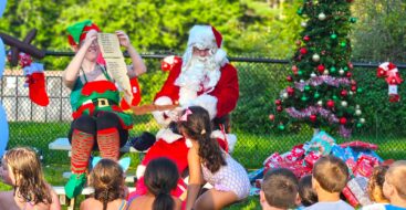 Santa and his elf reading a list off to a group of young campers