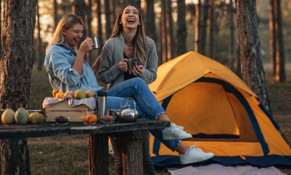 Female friends enjoying hot beverage while camping in the forest in the fall